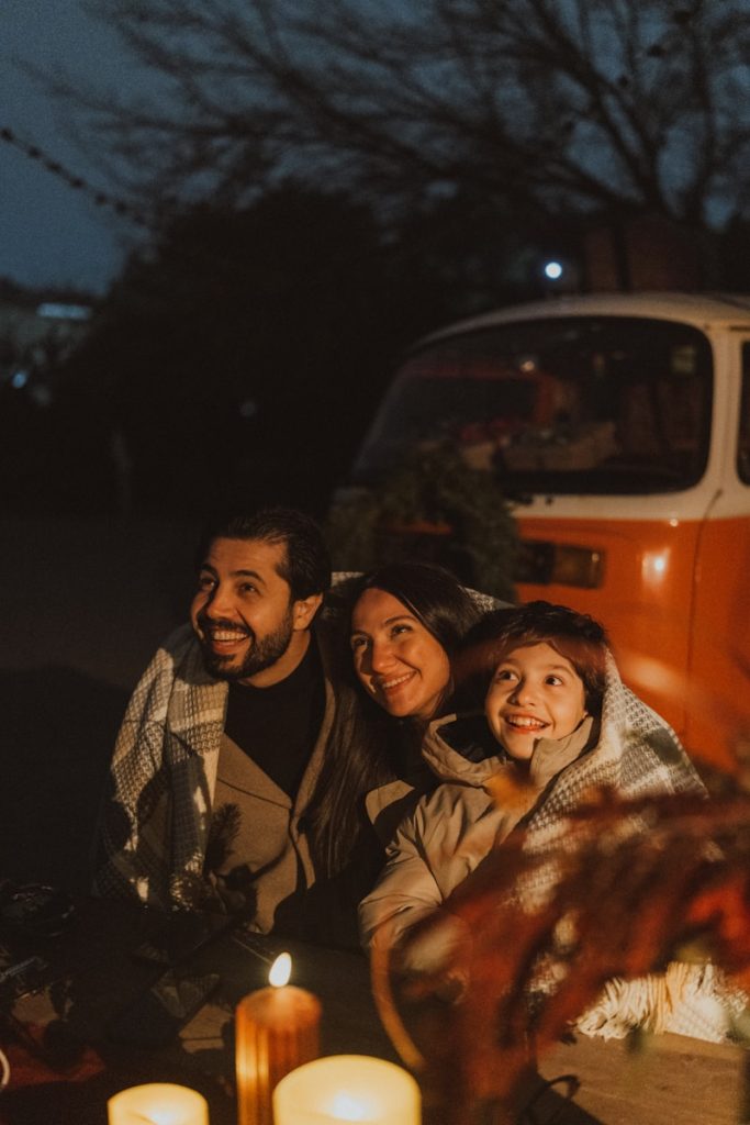 Family wrapped in blanket with camper van at night