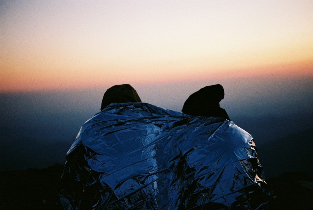 Best Double Sleeping Bags for Couples: Vetted Top 5 Coziest Picks person in blue jacket and black knit cap sitting on rock formation during daytime