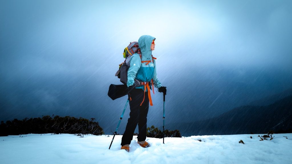A hiker stands in snow with a backpack and poles.