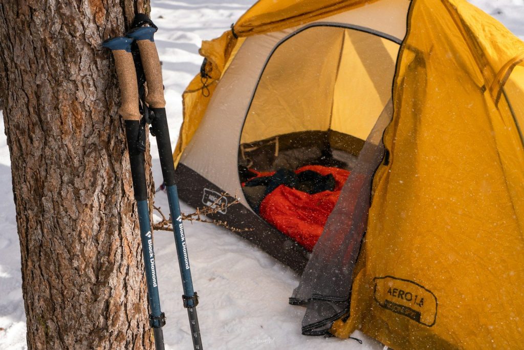 Best Sleeping Pads for Cold Ground: Vetted Sub-Zero Thermal Barriers a tent with a sleeping bag in the snow next to a tree